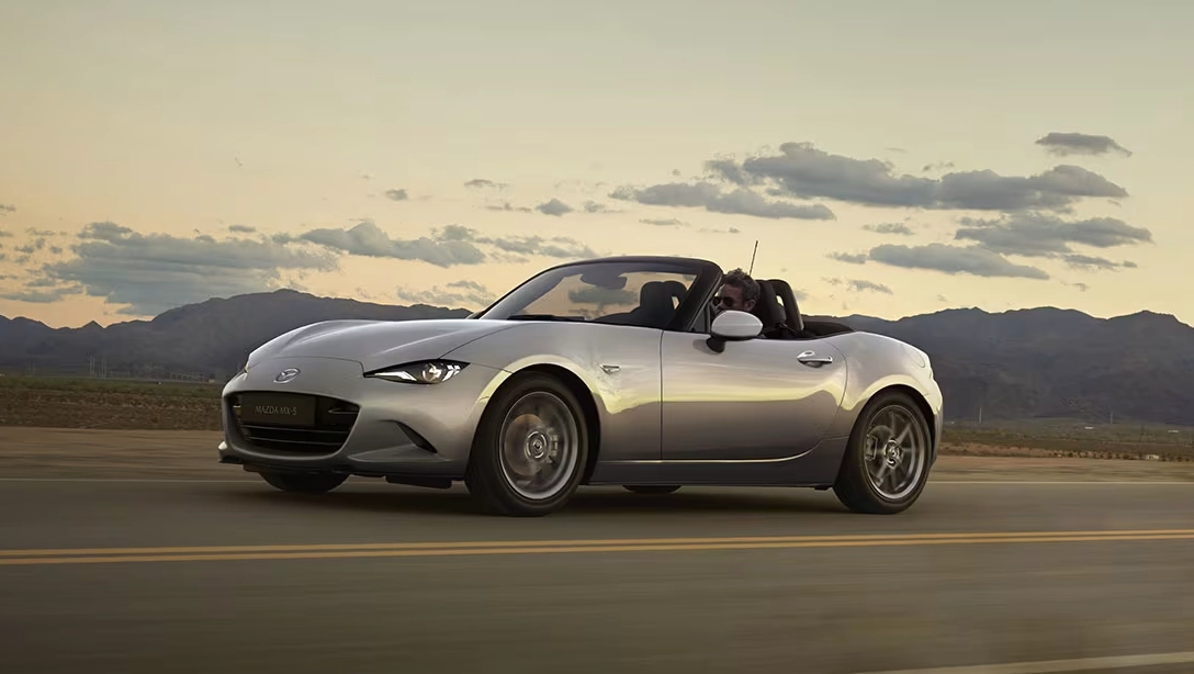 Vue dynamique de la Mazda MX-5 sur route sinueuse, capote ouverte